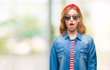 Genç güzel kadın yüzünden korkuyor ve şok sürpriz ifade, korku ve heyecan yüz ile güneş gözlüğü takıyor izole arka plan.