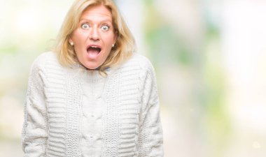 Orta yaş sarışın kadın giyiyor kış kazak korkuyor ve şok sürpriz ifade ile izole arka plan üzerinde korku ve yüz heyecanlı.