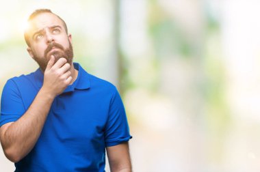 Üzerinde mavi gömlek giymiş genç beyaz hipster adam arka plan çene düşünme hakkında soru, dalgın ifade üzerine el ile izole. Düşünceli yüzüyle gülümsüyor. Şüphe kavramı.