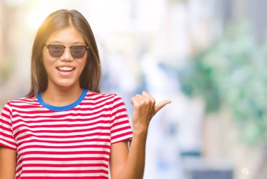 Genç Asyalı kadın arıyorum ve başparmak yanında yukarıyı mutlu yüz ile gülümseyen izole arka plan üzerinde güneş gözlüğü takıyor.