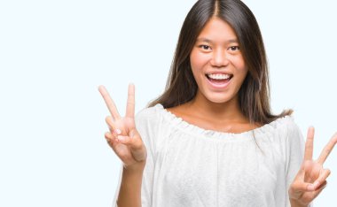 Genç Asyalı kadın parmaklarını zafer işareti yaparken gösterilen kamera seyir gülümseyen izole arka plan üzerinde. İki numaralı.