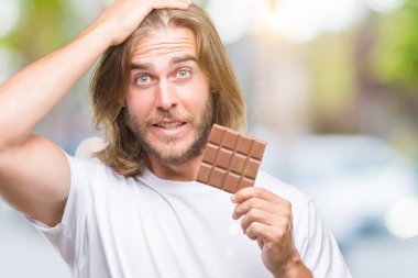 Baş, el ile vurguladı izole arka plan üzerinde çikolata yeme uzun saçlı Genç yakışıklı adam şok utanç ve sürpriz suratla, öfkeli ve sinirli. Korku ve hata için üzgün.