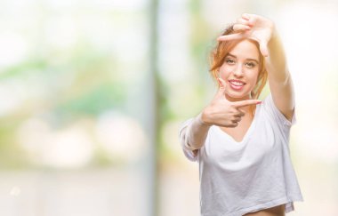 Genç güzel kadın elle yapma çerçeve ve parmakları ile mutlu yüz gülümseyen izole arka plan yüzünden. Yaratıcılık ve Fotoğrafçılık kavramı.