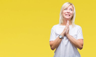 Yalvarıyor ve umut ifade yüzünde çok duygusal ve endişe ile birlikte elleriyle dua izole arka plan üzerinde beyaz t-shirt giyen genç güzel sarışın bir kadın. Bağışlanmak. Din kavramı.