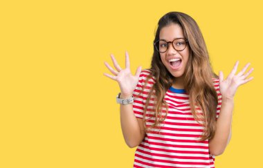 Genç güzel esmer kadın gözlük ve çizgili t-shirt üzerine arka plan çılgın ve çığlık kaldırdı ve açık gözleri heyecanlı silah ile başarı için hayran kutluyor izole. Kazanan kavramı