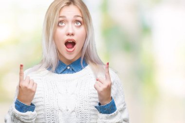 İzole arka plan üzerinde kış kazak giyen genç sarışın kadın hayrete ve yukarıya bakıp parmakları ile işaret şaşırttı ve silah kaldırdı.