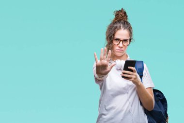 Sırt çantası, kulaklık ve akıllı telefon açık eliyle dur işareti ile ciddi ve kendine güvenen ifade, savunma jest yapıyor izole arka plan üzerinde giyen genç esmer öğrenci kız