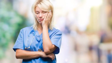 Düşünme izole arka plan bakmaktan Tıbbi üniforma giyen genç güzel sarışın doktor kadın yorgun ve sıkılmış çapraz silah depresyon sorunları ile.