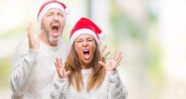 Orta yaş İspanyol çift üzerinde Noel şapka arka plan deli izole ve deli bağırarak ve agresif ifade ve silah kaldırdı bağırıyor. Hayal kırıklığı kavramı.