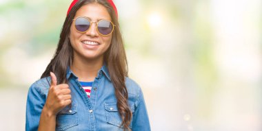 Genç güzel Arap kadın hareketi el ile mutlu yaşasın yapıyor izole arka plan üzerinde güneş gözlüğü takıyor. Kameraya bakarak başarı gösteren ile ifade onaylama.