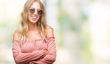 Güzel genç sarışın kadın üzerinde Retro güneş gözlüğü takıyor mutlu yüz ile gülümseyerek kameraya seyir silah geçti arka plan izole. Olumlu bir kişi.