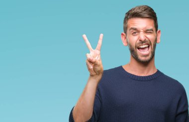 Mutlu yüz zafer işareti yaparken kameraya göz kırpıyor ile gülümseyen izole arka plan üzerinde kış kazak giyen genç yakışıklı adam. İki numaralı.