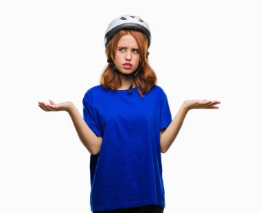 İzole arka plan clueless ve şaşkın bir ifadeyle kollar ve eller kaldırdı üzerinde bisikletçi kask giyen genç güzel kadın. Şüphe kavramı.