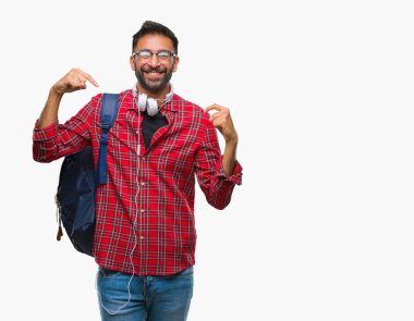 Yüzünde gülümseme ile kendinden emin görünüyorsun, kendini gururlu ve mutlu parmakları ile işaret arka plan üzerinde kulaklık ve sırt çantası giyiyor yetişkin İspanyol öğrenci adam izole.