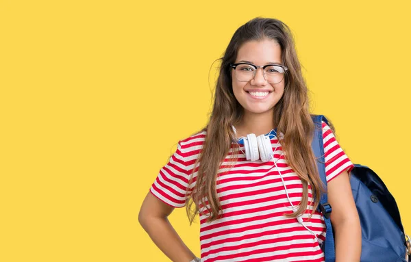 美しいブルネットの学生の若い女性の顔に幸せとクールな笑顔で孤立した背景にヘッドフォンとバックパックを着用します 幸運な人 — ストック写真
