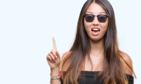 Mladá Asijská Žena Nosí Sluneční Brýle Přes Izolované Pozadí Ukazováčkem — Stock fotografie