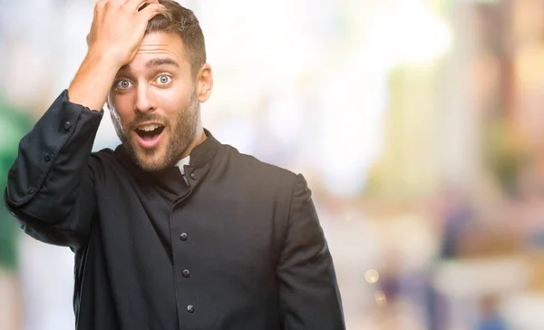 Young catholic christian priest man over isolated background surprised with hand on head for mistake, remember error. Forgot, bad memory concept.