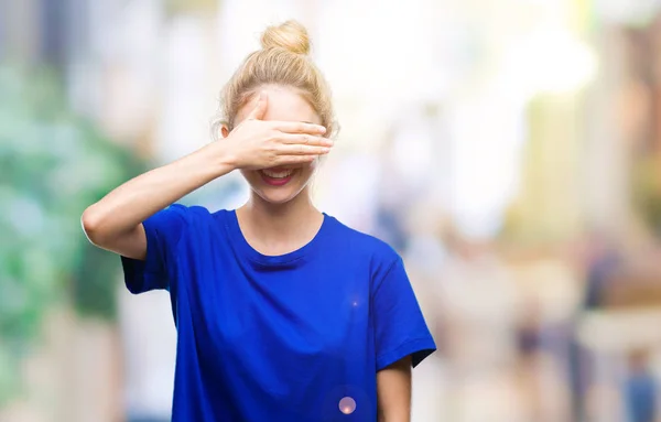 Young beautiful blonde and blue eyes woman wearing blue t-shirt over isolated background smiling and laughing with hand on face covering eyes for surprise. Blind concept.