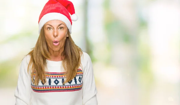 Middle age adult woman wearing winter sweater and chrismat hat over isolated background afraid and shocked with surprise expression, fear and excited face.