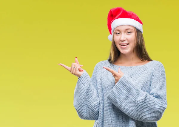 年轻美丽的白种人妇女戴着圣诞节帽子在孤立的背景微笑 看着相机指着两个手和手指到一边 — 图库照片