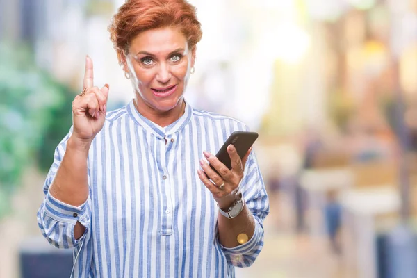 Atrractive senior caucasian redhead woman texting using smartphone over isolated background surprised with an idea or question pointing finger with happy face, number one