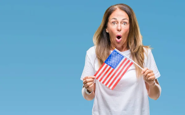 Middle age hispanic woman holding flag of United States of America over isolated background scared in shock with a surprise face, afraid and excited with fear expression