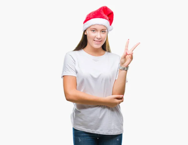 若い美しい白人女性の勝利のサインを行うカメラでウィンクしている幸せそうな顔を浮かべて隔離された背景にクリスマス帽子をかぶっています — ストック写真