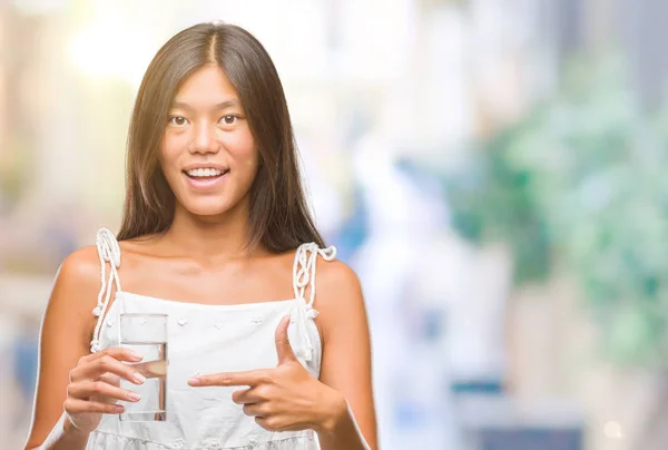 Young asian woman drinking glass of water over isolated background very happy pointing with hand and finger