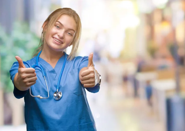 若い白人の医者の女性の手で肯定的なジェスチャーをして承認する分離の背景の上の外科医の制服を着て笑顔と幸せな成功のための親指します カメラ 勝者のジェスチャーを見てください — ストック写真