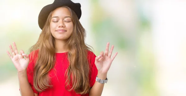 年轻美丽的黑发时尚女人穿着红色 T恤和黑色贝雷帽在孤立的背景放松和微笑闭着眼睛做冥想手势用手指 瑜伽概念 — 图库照片
