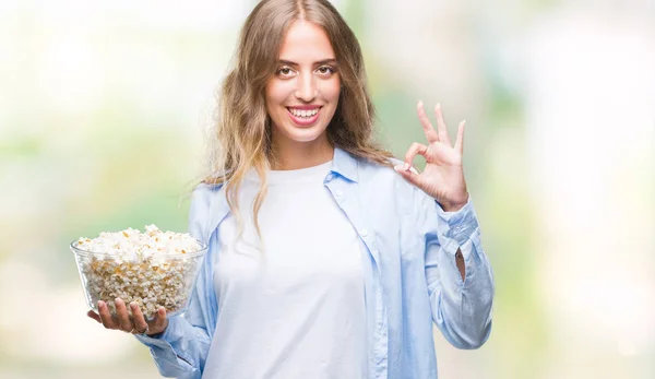 美丽的年轻金发碧眼的女人吃爆米花在孤立的背景做确定的标志与手指 优秀的象征 — 图库照片