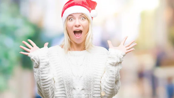 年轻美丽的金发女子戴着圣诞节帽子在孤立的背景庆祝疯狂和惊讶的成功与双臂举起和睁开的眼睛尖叫兴奋 获奖者概念 — 图库照片