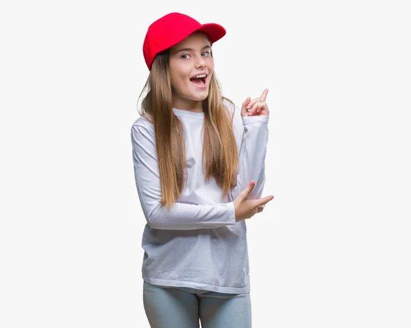 赤い帽子を身に着けている美しい少女分離背景の顔に大きな笑みを浮かべてカメラを見ている側の手と指で指す — ストック写真