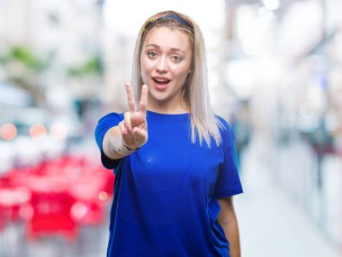 Genç Sarışın kadın mutlu yüz zafer işareti yaparken kameraya göz kırpıyor ile gülümseyen izole arka plan yüzünden. İki numaralı.