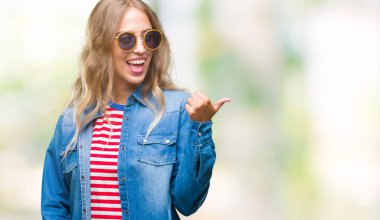 Güzel genç sarışın kadın arıyorum ve başparmak yanında yukarıyı mutlu yüz ile gülümseyen izole arka plan üzerinde güneş gözlüğü takıyor.