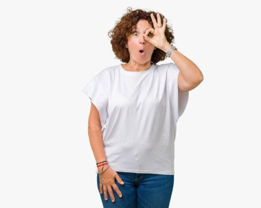 Sürpriz yüz, göz parmaklarının arasından seyir ile ok jest yapıyor izole arka plan üzerinde beyaz t-shirt giyen kadın güzel orta ager kıdemli şok. İmansız ifade.