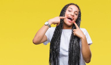 Genç saç Afro-Amerikan Kız kendinden emin gösterilen ve işaret parmakları diş ve ağız ile gülümseyen izole arka plan üzerinde örgülü. Sağlık kavramı.