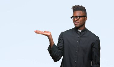 Genç Afro-Amerikan rahip adam neşeli sunulması ve kameraya bakarak avucunun ile işaret gülümseyen izole arka plan.