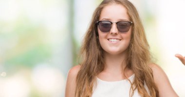 Gülümseyen güneş gözlüğü ve süre seyir ve kamera boyutu işaret parmaklarıyla yapıyor el ile kendine güvenen el hareketi giyen genç sarışın kadın. Ölçü kavramı.