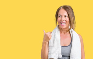 Seyir ve başparmak yanında yukarıyı mutlu yüz ile gülümseyen izole arka plan üzerinde spor giyim ve havlu giyen güzel orta yaş kadın.