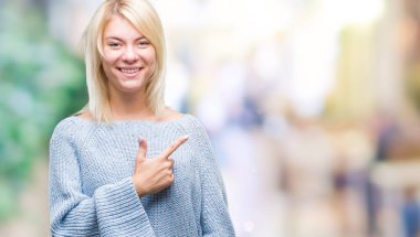 İzole arka neşeli bir gülümseme ile el ve parmak kadar kameraya bakarak yüzündeki mutlu ve doğal ifade ile yan ile işaret yüz üzerinden kış kazak giyen genç güzel sarışın kadın.