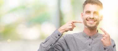 Kendinden emin gösterilen ve işaret parmakları diş ve ağız ile gülümseyen genç hipster adam. Sağlık kavramı.