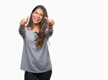 Genç güzel Arap kadın el ile pozitif jest yapıyor onaylama izole arka plan üzerinde güneş gözlüğü takıyor başparmak gülümseyen ve başarı için mutlu. Kamera, kazanan jest arıyorsunuz.