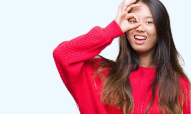 Gülümseyerek el parmakları ile mutlu yüz üzerinden seyir göz ile ok jest yapıyor izole arka plan üzerinde kış kazak giyen genç Asyalı kadın.
