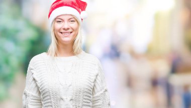 Yüzünde mutlu ve güzel bir gülümseme ile izole arka plan üzerinde Noel şapka giyen genç güzel sarışın kadın. Şanslı kişi.