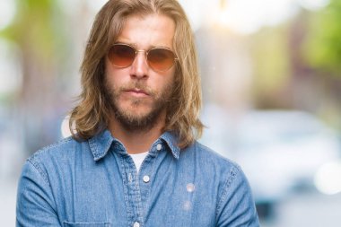 Genç yakışıklı adam uzun saçlı izole arka plan şüpheci ve sinir, onaylamayan ifade yüz çapraz kolları üzerinde güneş gözlüğü takıyor. Negatif kişi.