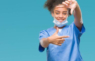 Genç afro Amerikalı doktor kadın elle yapma çerçeve ve parmakları ile mutlu yüz gülümseyen izole arka plan yüzünden. Yaratıcılık ve Fotoğrafçılık kavramı.