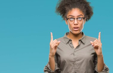 Genç afro Amerikalı kadın hayrete ve yukarıya bakıyor ve parmakları ile işaret ve silah kaldırdı sürpriz izole arka plan üzerinde gözlük.