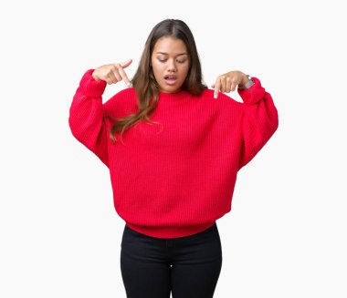 Üzerinde izole kırmızı kış kazak giyen genç güzel esmer kadın arka plan işaretleme aşağı reklam, sürpriz yüz ve açık ağız gösterilen parmakları ile