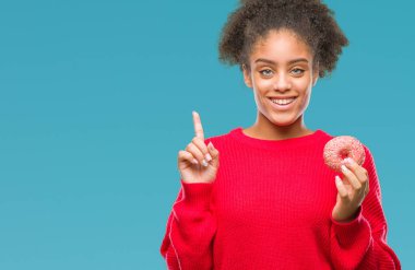 Genç afro Amerikalı kadın izole arka bir fikir ya da soru işaret parmağı gülen yüz, bir numara ile sürpriz üzerinde donut yemek